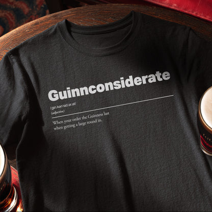 Black t-shirt with white text on a wooden pub table with pints of Guinness. Guinnconsiderate :: When you order the Guinness last when getting a big round in.