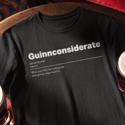 Black t-shirt with white text on a wooden pub table with pints of Guinness. Guinnconsiderate :: When you order the Guinness last when getting a big round in.