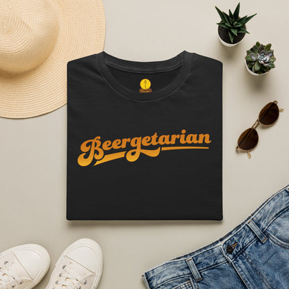 A folded black T-shirt with the word 'Beergetarian' printed in a retro orange-yellow script across the chest, styled in a flat lay with a straw hat, white sneakers, blue jeans, sunglasses, and small potted succulents on a light beige background.