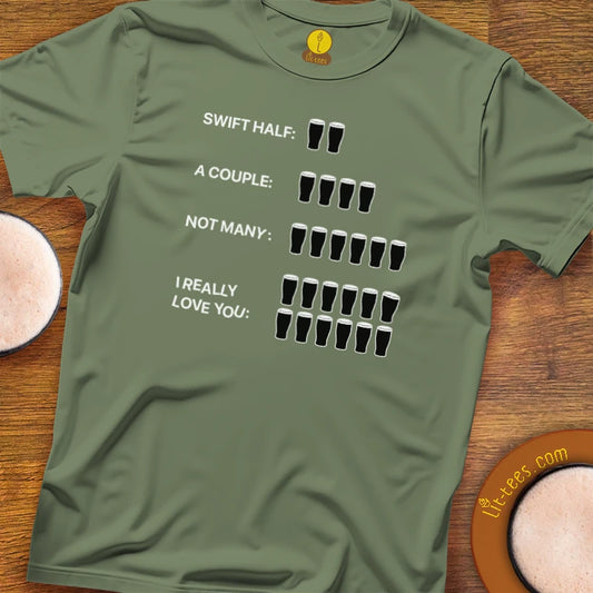 An Military Green green crewneck t-shirt with a humorous beer-themed graphic, laid flat on a wooden surface next to two pints of beer. The graphic reads 'SWIFT HALF: 2 glasses, A COUPLE: 4 glasses, NOT MANY: 8 glasses, I REALLY LOVE YOU: 16 glasses'.