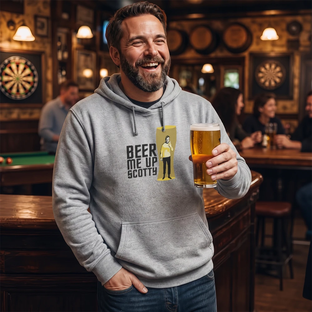 A man in a light gray hoodie stands in a dimly lit bar holding a glass of beer. The hoodie features a graphic print that reads 'BEER ME UP SCOTTY' next to a yellow figure.