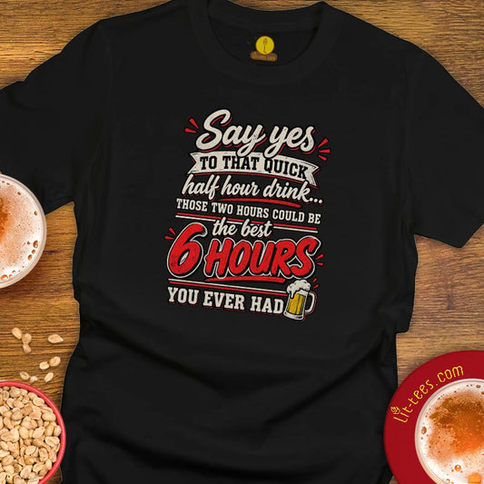 A black short-sleeve graphic t-shirt laid flat on a wooden surface, reading 'Say yes to that drink... Those 2 hours could be the best 6 hours you ever had