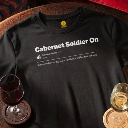 Black t-shirt with 'Cabernet Soldier On' text and wine glasses on a wooden bar table.