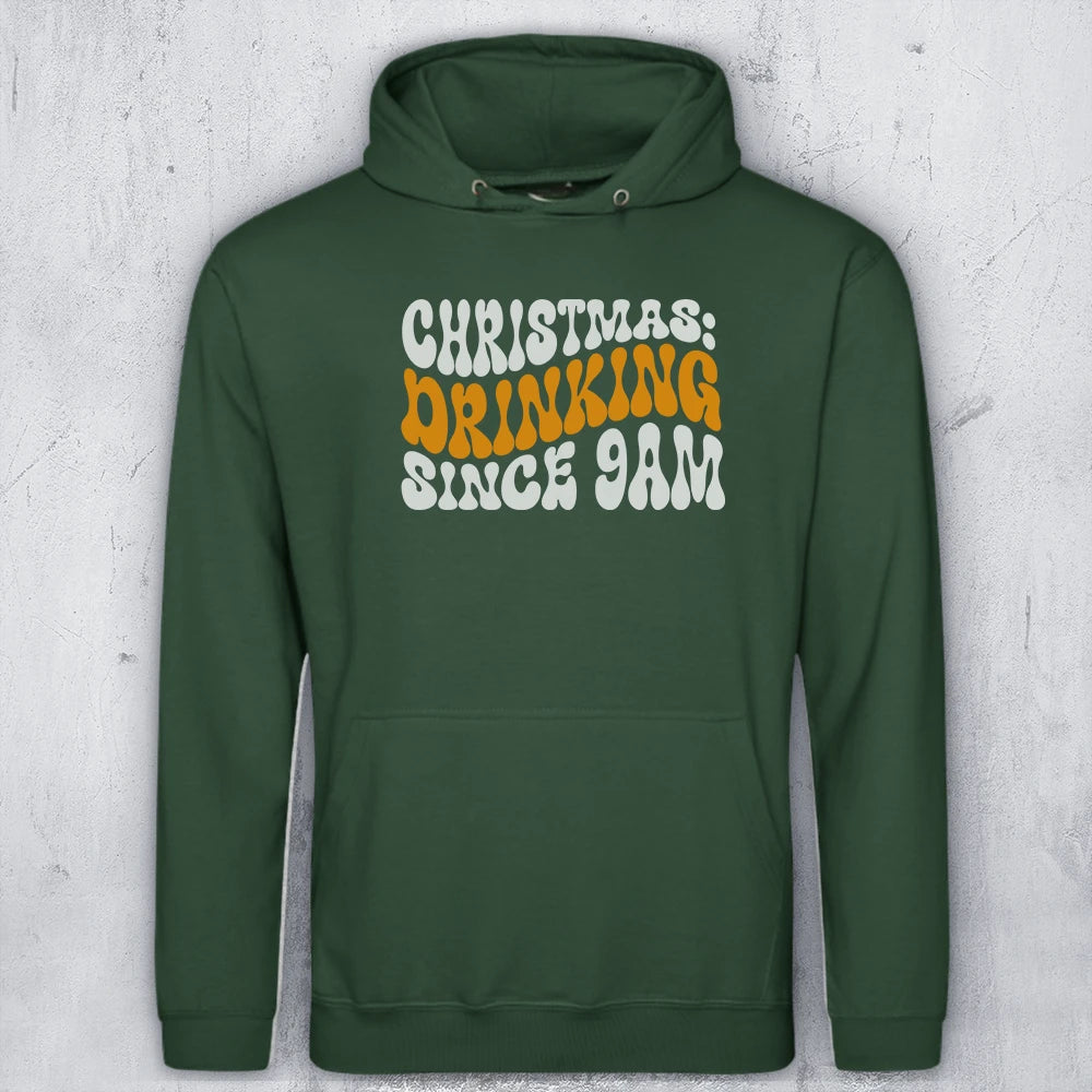 A dark green pullover hoodie with a front graphic reading 'CHRISTMAS DRINKING SINCE 9AM' in white and orange lettering, displayed against a light gray textured background.