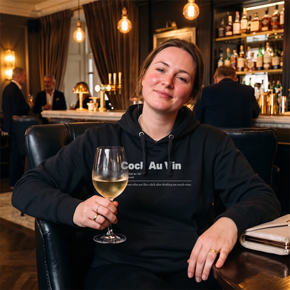 A woman sitting in a dimly lit bar or lounge, wearing a black hoodie with the text 'Sauvignon Blank' printed on the chest, and holding a glass of white wine.