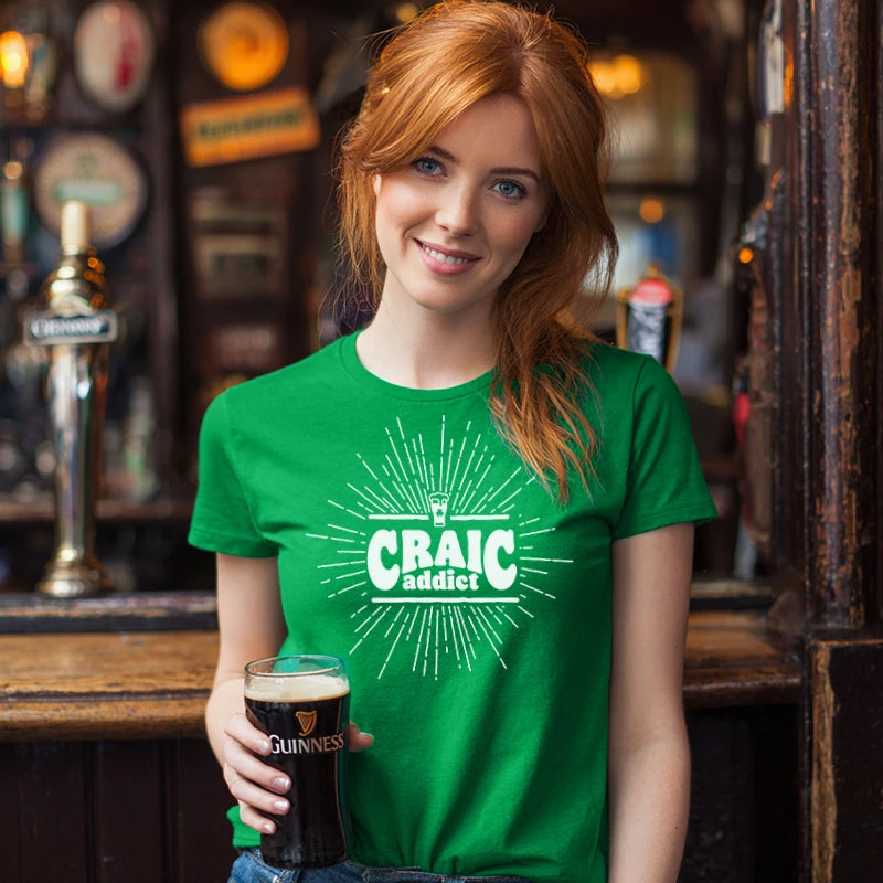 Woman wearing a green 'Craic Addict' t-shirt holding a glass of Guinness in a bar.