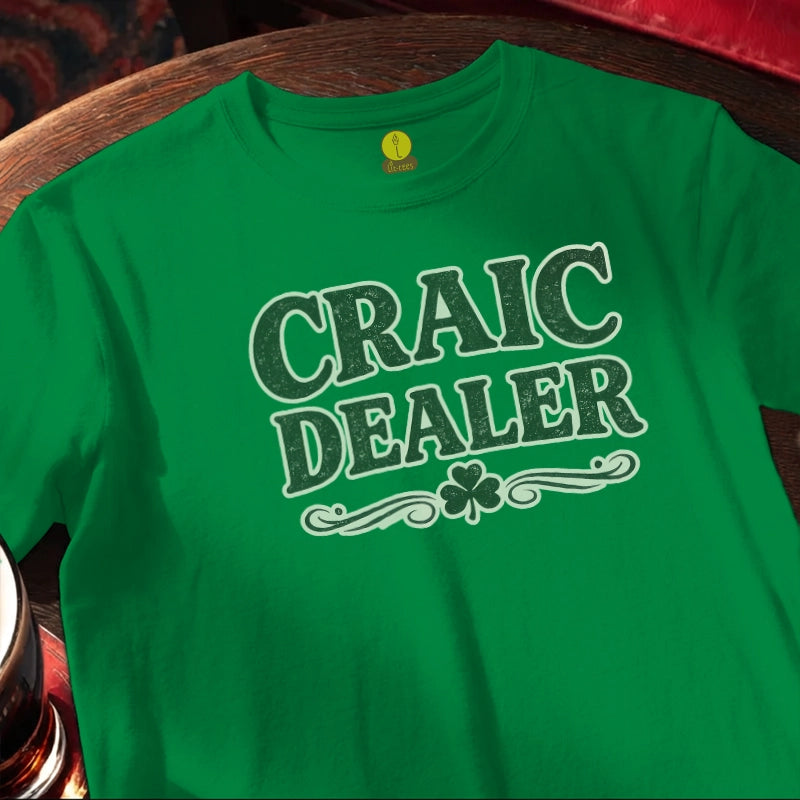 Green t-shirt with 'Craic Dealer' text and shamrock on a wooden bar table