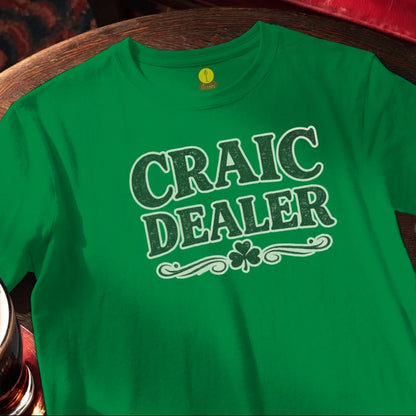 Green t-shirt with 'Craic Dealer' text and shamrock on a wooden bar table