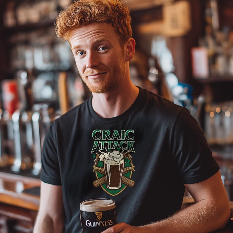 Man wearing a black t-shirt with 'Craic Attack' design, holding a Guinness beer glass in a bar setting.