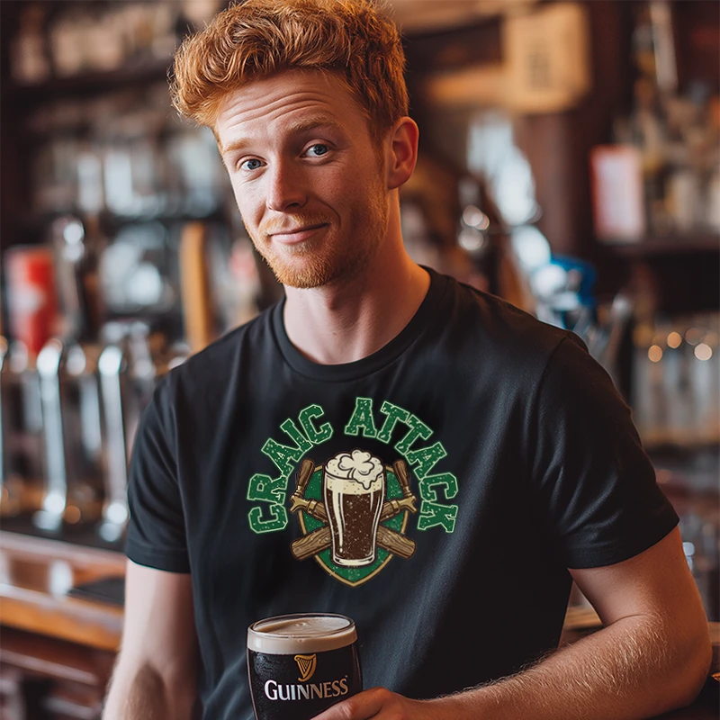 Man wearing a black t-shirt with 'Craic Attack' design, holding a pint of Guinness  in a bar setting.