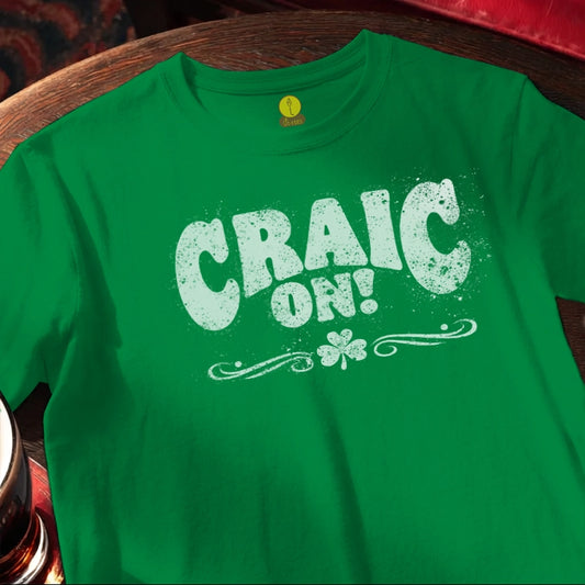Green t-shirt with 'CRAIC ON!' text and shamrock design on a wooden bar table