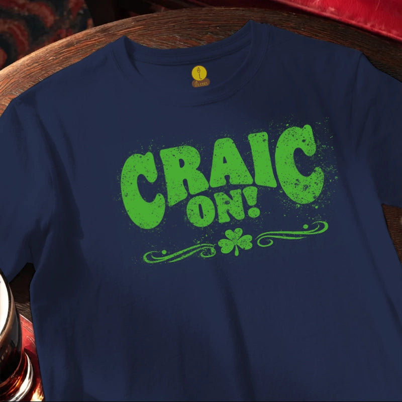 Blue t-shirt with green 'CRAIC ON!' text and shamrock on a wooden surface.