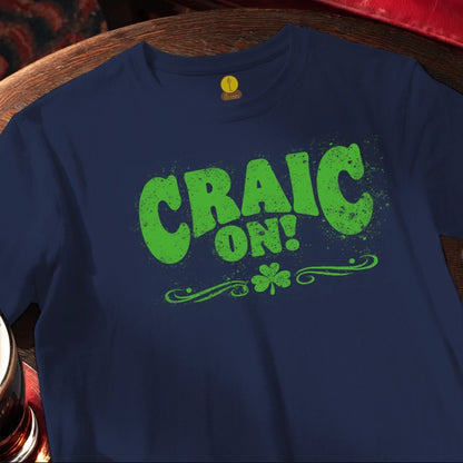 Blue t-shirt with green 'CRAIC ON!' text and shamrock on a wooden surface.