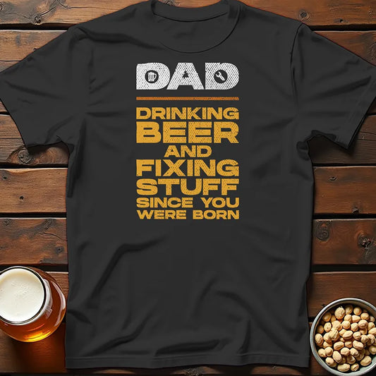 Black Father's Day t-shirt with yellow text on a wooden surface with a beer mug and bowl of nuts.