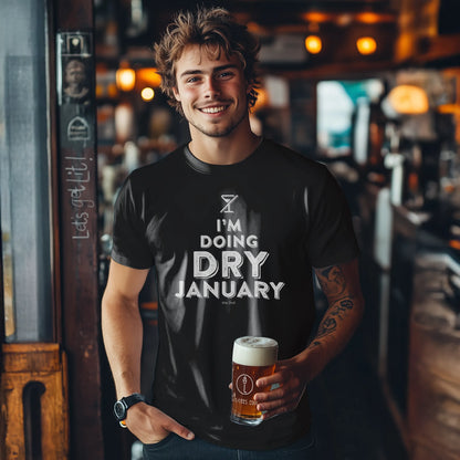 Man wearing a 'I'm Doing Dry January' t-shirt holding a beer in a bar.