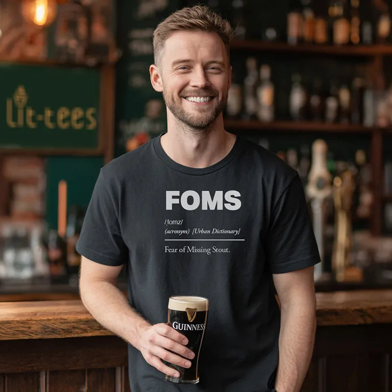 Man holding a Guinness wearing a black t-shirt with 'FOMS - Fear of Missing Stout' definition text in a pub setting