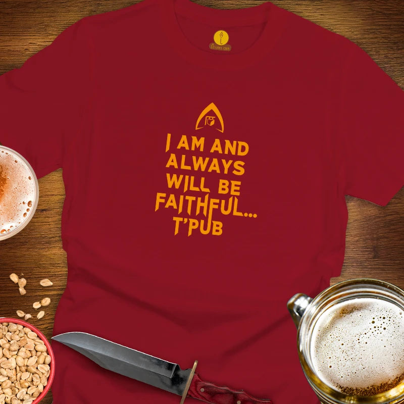 A red graphic t-shirt laid flat on a wooden surface, surrounded by beer mugs, peanuts, and a knife. The shirt features a yellow Star Trek-style delta insignia and the text 'I AM AND ALWAYS WILL BE FAITHFUL T'PUB'.