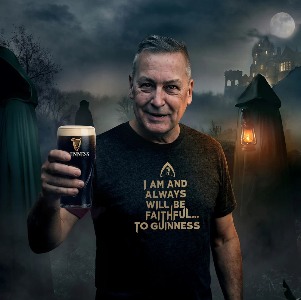 A man wearing a black Guinness t-shirt with a gold slogan stands in a spooky, foggy Halloween-themed setting, holding up a pint of Guinness. Tee shirt reads' 'I am and always will be faithful to Guinness.'