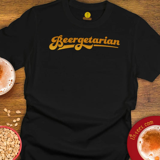 A black short-sleeve t-shirt laid flat on a wooden surface, featuring the word 'Beergetarian' printed across the chest in a yellow-gold cursive font. The shirt is styled with beer glasses, peanuts, and a red coaster in the corners.