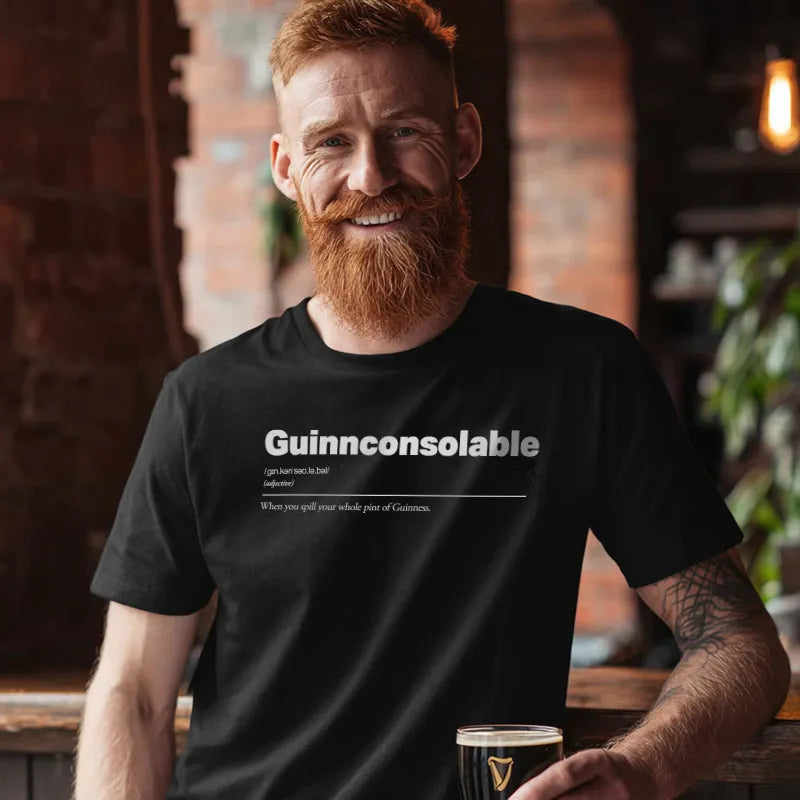 Man wearing a black t-shirt with 'Guinnconsolable' text, holding a pint glass in a bar setting. Guinnconsolable :: When you spill your whole pint of Guinness.