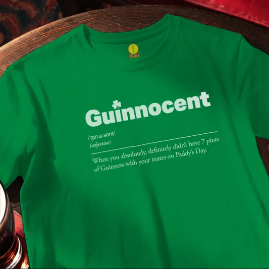 Green t-shirt with 'Guinnocent' text on a wooden bar table with beer glass.