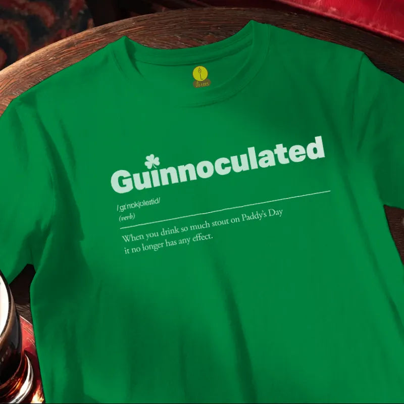 Green t-shirt with 'Guinnoculated' text on a wooden bar table.