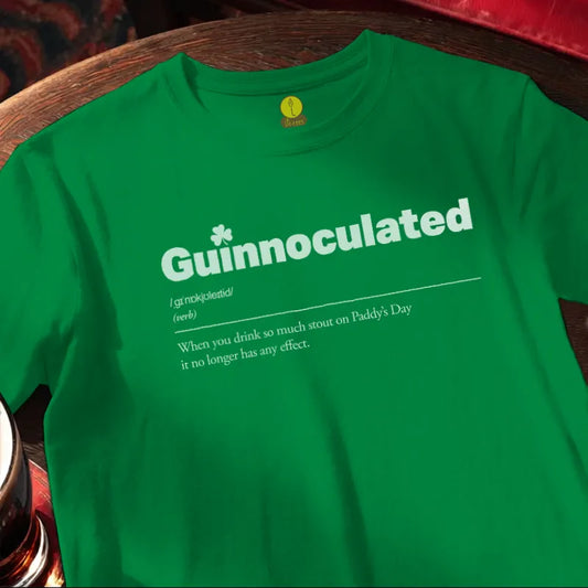 Green t-shirt with 'Guinnoculated' text on a wooden bar table.