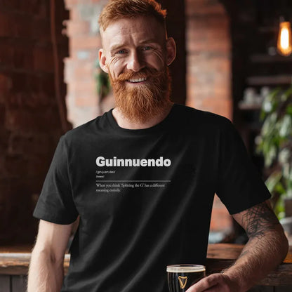 Man wearing a black t-shirt with 'Guinnuendo' text, holding a glass in a bar setting. Guinnuendo :: When you think 'Splitting the G' has a different meaning entirely.