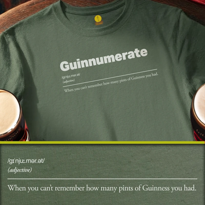 A dark green t-shirt with a humorous Guinness-themed dictionary definition printed on the chest reading 'Guinnumerate'. When you can't remember how many pints of Guinness you had. The shirt is styled on a wooden surface with two pint glasses partially visible on either side, and a digital text overlay at the bottom showing the pronunciation and definition.