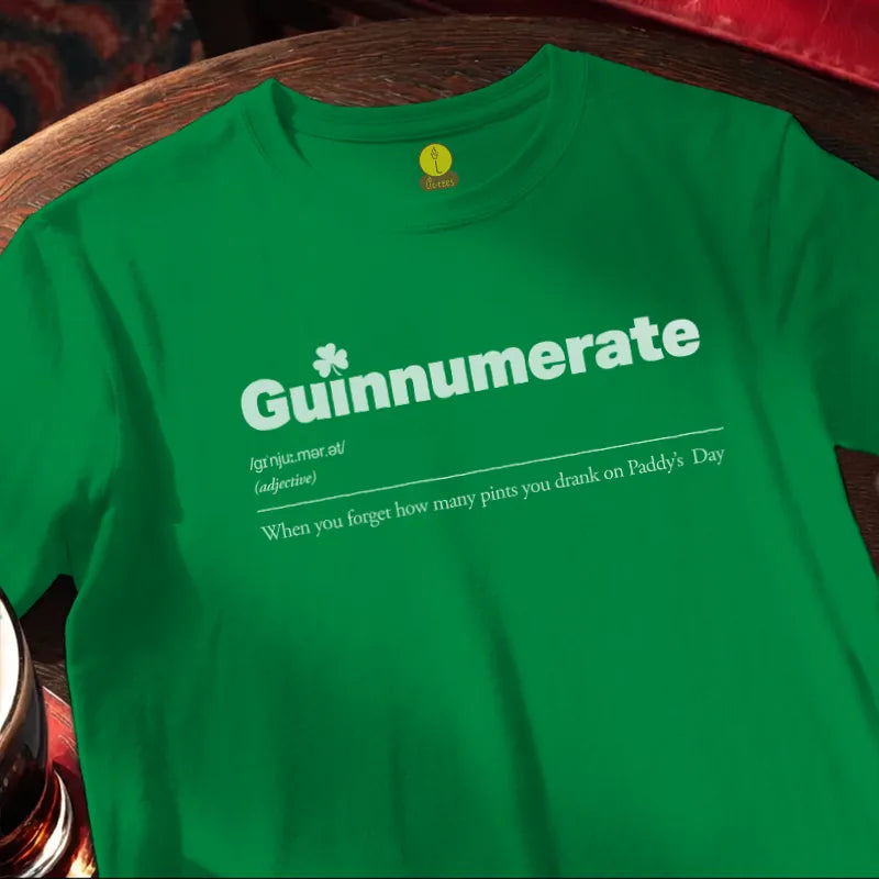 Green St Patrick's Day tee shirt with 'Guinnumerate. When you forget how many pints you drank on Paddy’s Day.' text on a wooden bar table with beer glass.