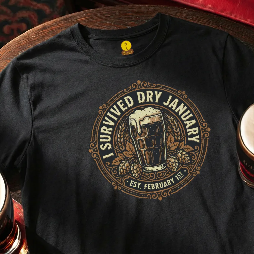 Black t-shirt with 'I Survived Dry January' design featuring a beer glass and hops, placed on a wooden bar table.