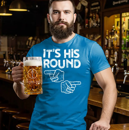 Man in a bar wearing a blue t-shirt with 'It's His Round' text, holding a beer mug.
