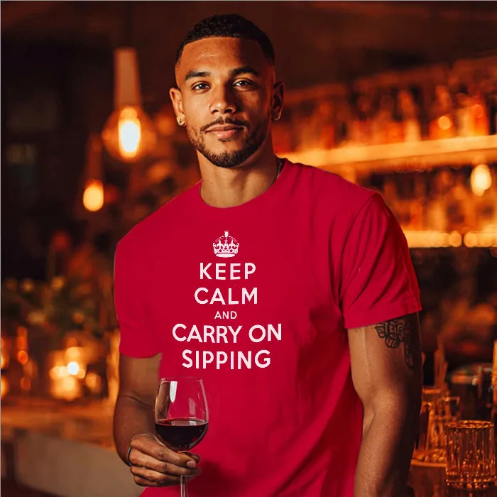 Man in bar holding wine glass wearing red t shirt with humourous text saying Keep Calm and Carry on Sipping