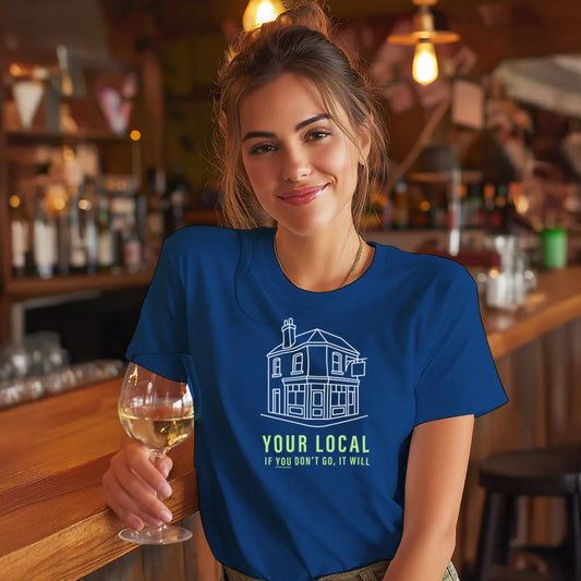 Woman in a bar wearing a blue t-shirt with a pub graphic and text saying 'Your local, if you don't go, it will' , holding a glass of wine.