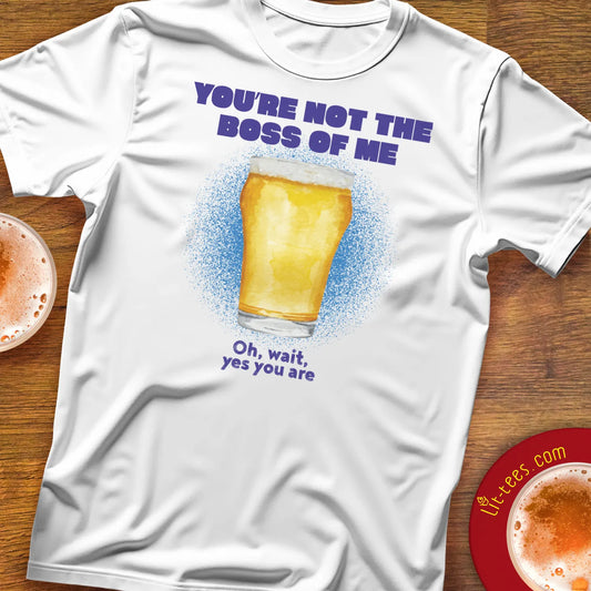 White t-shirt saying 'You're not the boss of me' with a beer graphic and text on a wooden surface with drinks.