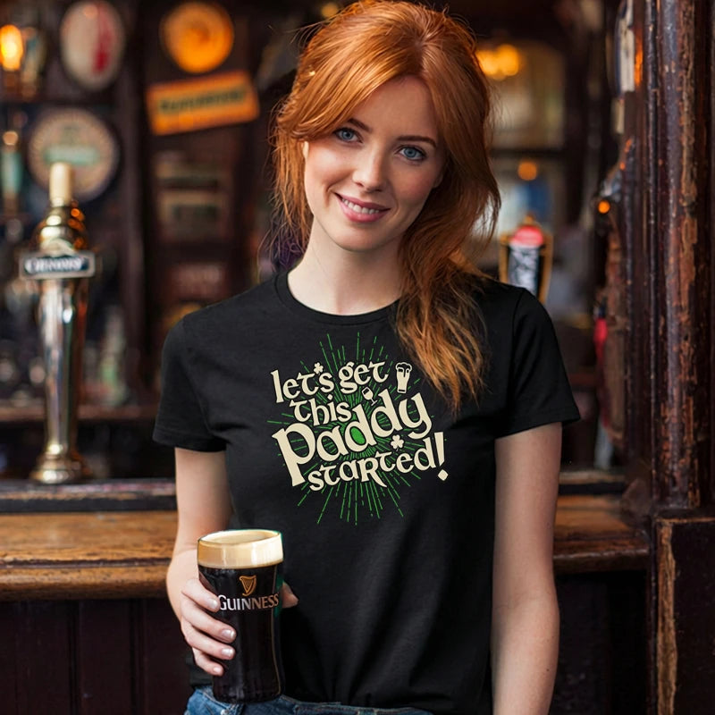 Woman in a bar holding a pint of Guinness wearing a black t-shirt with text saying 'Let's Get this Paddy Started'