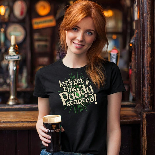 Woman in a bar holding a pint of Guinness wearing a black t-shirt with text saying 'Let's Get this Paddy Started'