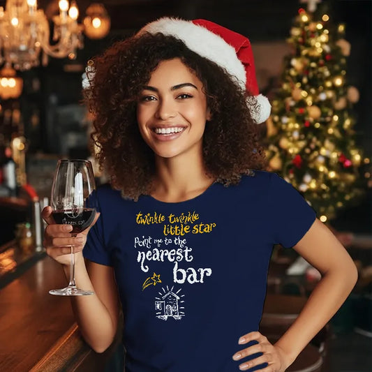 Woman wearing a Santa hat and blue t-shirt reading 'Twinkle twinkle little star, point me to the nearest bar' with a Christmas-themed quote, holding a glass of wine in a festive bar setting.