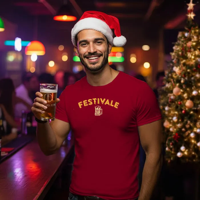 Man in a red Christmas themed 'Festivale' t-shirt and Santa hat holding a beer in a festive bar setting. Glass has lit-tees.com printed on it.