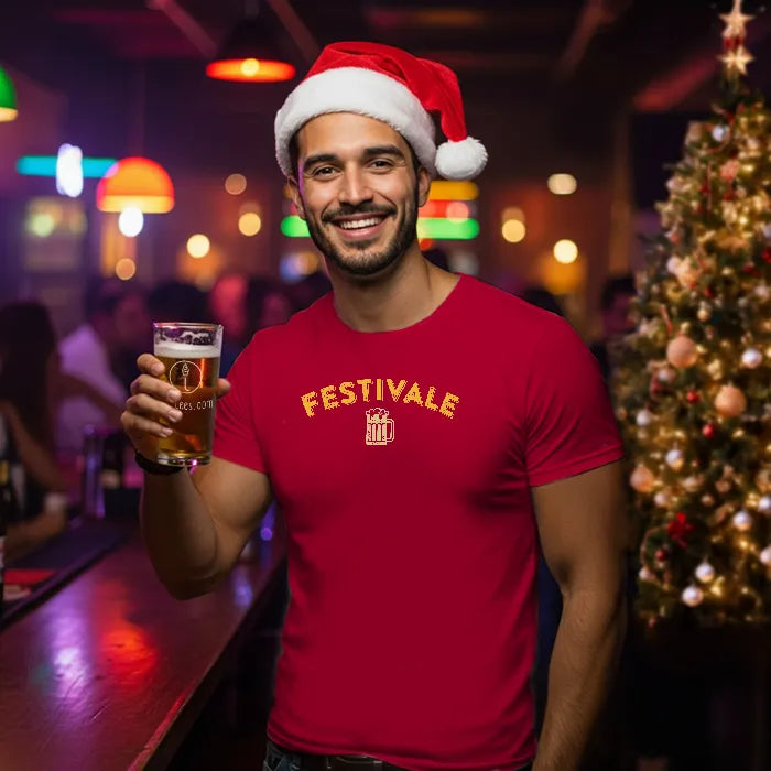 Man in a red Christmas themed 'Festivale' t-shirt and Santa hat holding a beer in a festive bar setting. Glass has lit-tees.com printed on it.