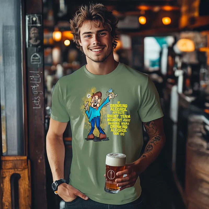 Young man holding a beer in a bar wearing a green tee shirt with a graphic character and humorous text saying 'If drinking alcohol affects short term memory just imagine what drinking alcohol can do' 