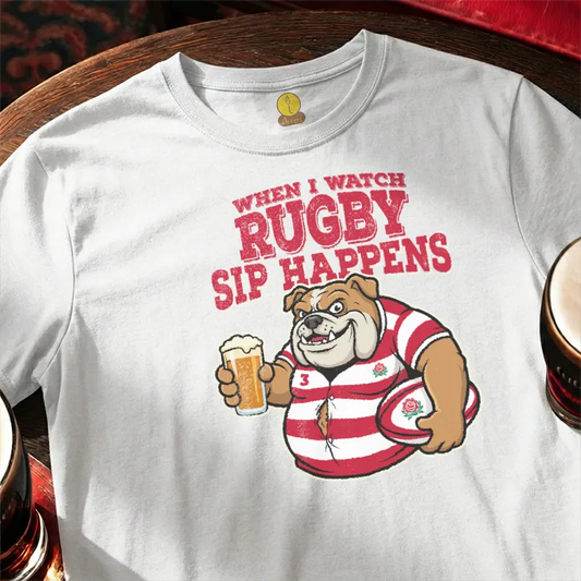 White t-shirt with rugby-themed graphic and text  saying 'When I watch Rugby, Sip happens' on a wooden bar table