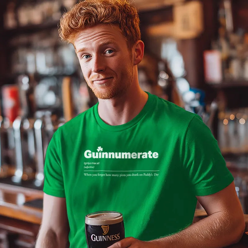 Man wearing a green 'Guinnumerate' t-shirt holding a Guinness in a bar setting.