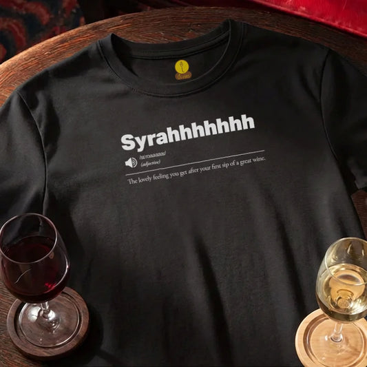 Black t-shirt with 'Syrahhhhhh' text on a wooden bar table with wine glasses.