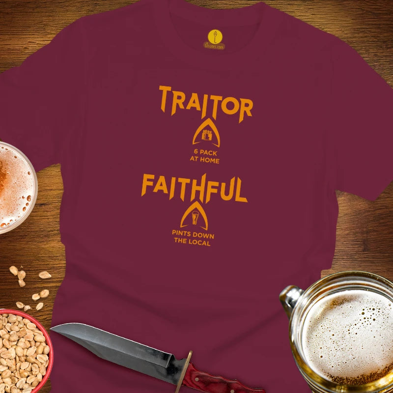 A maroon short-sleeve t-shirt laid flat on a wooden surface, featuring orange text that reads 'TRAITOR FAITHFUL' with small logo graphics and phrases underneath. The shirt is styled with beer glasses, peanuts, and a knife around it.