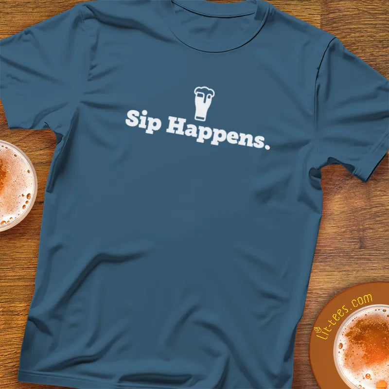 Indigo blue t-shirt with 'Sip Happens.' text on a wooden surface with drinks.