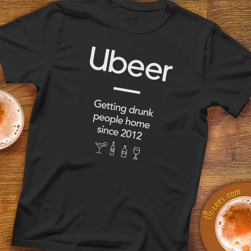 Black t-shirt with 'Ubeer' text and graphics on a wooden surface with drinks.