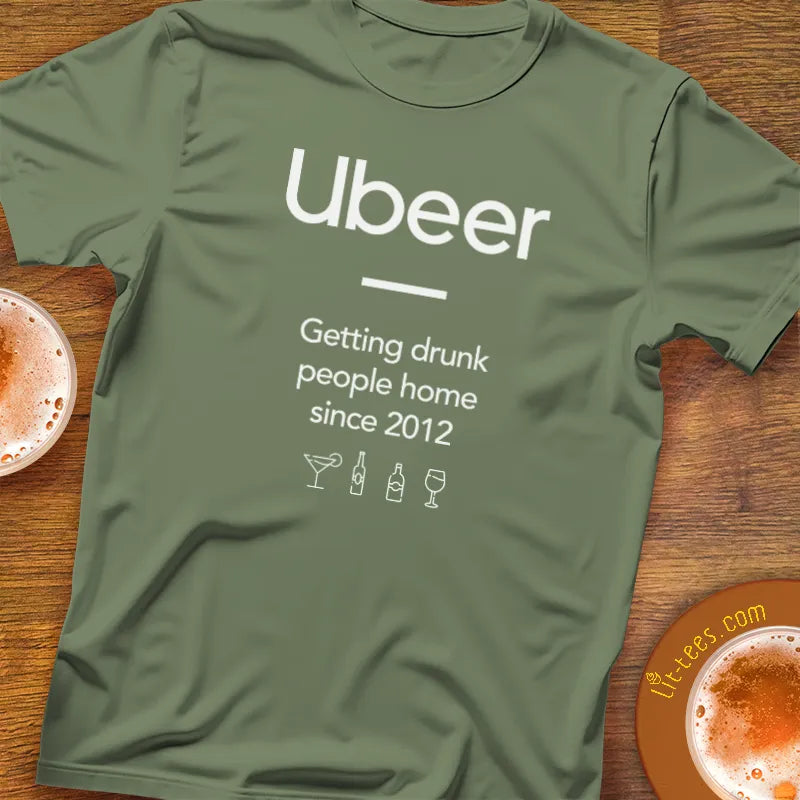 Green t-shirt with 'Ubeer' text and graphics on a wooden surface with drinks.