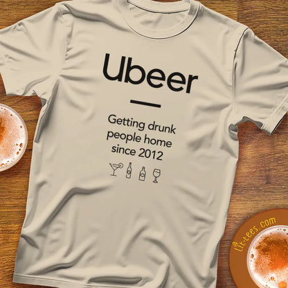 Gray t-shirt with 'Ubeer' text and graphics on a wooden surface with drinks.