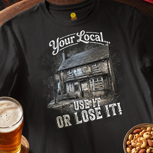 Black t-shirt with a graphic design and text, saying 'Your local use it or lose it' placed on a wooden surface with a glass of beer and bowl of nuts.